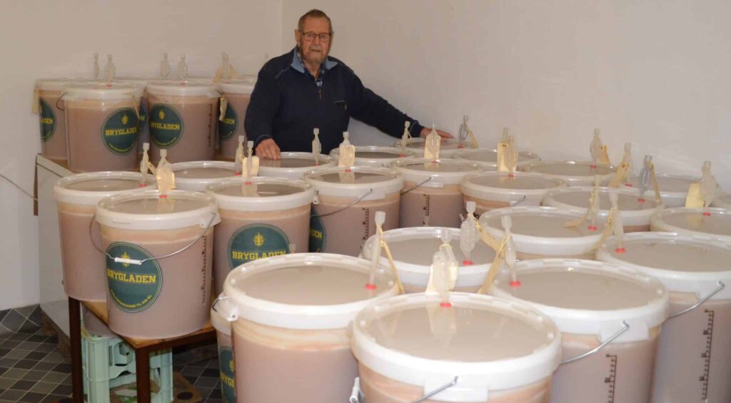 Svend står i sit mjødlokale ved siden af store tønder med flaskeklar Læsø Mjød, produceret af lokal lyng- og hindebægerhonning.